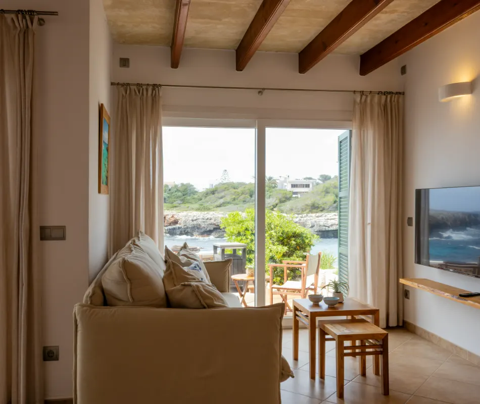 Sala luminosa con vista a la terraza y al mar, decorada con muebles de madera.