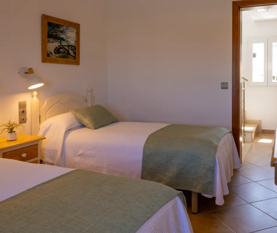 Habitaci&oacute;n con dos camas, l&aacute;mpara y cuadro en la pared.