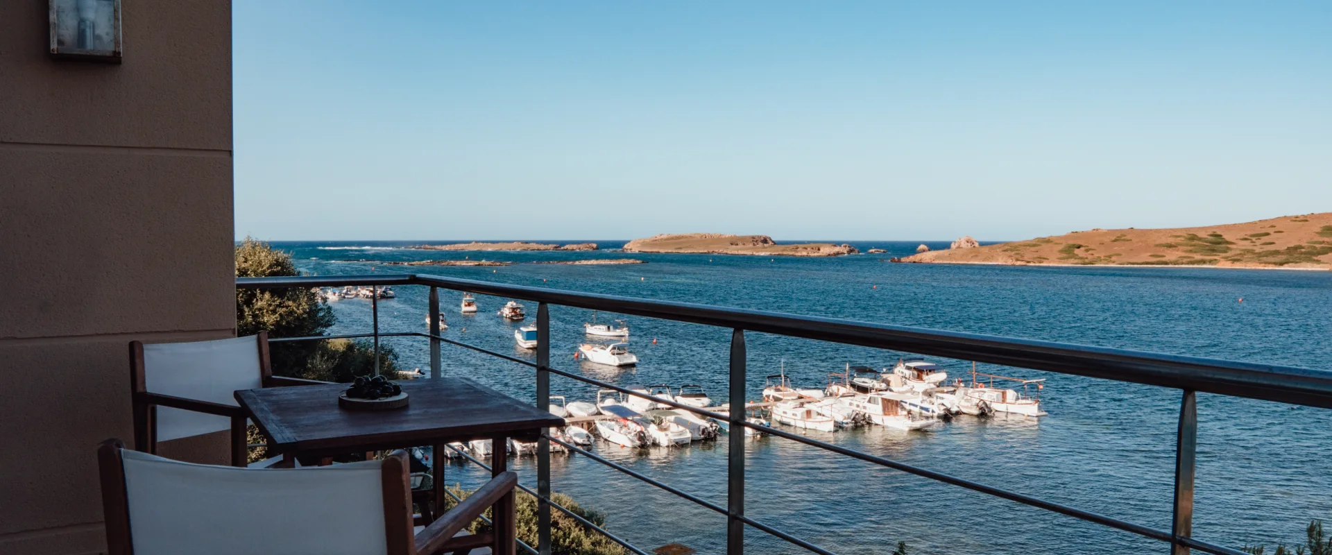 Balc&oacute;n con vista al mar y barcos anclados bajo un cielo despejado.