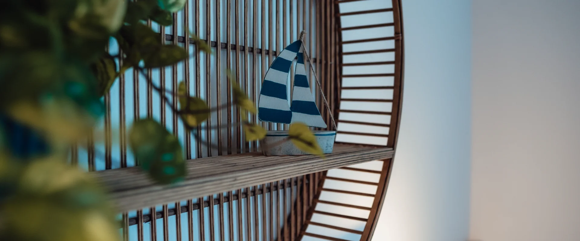 Estante con barco de vela azul y blanco, rodeado de hojas verdes.