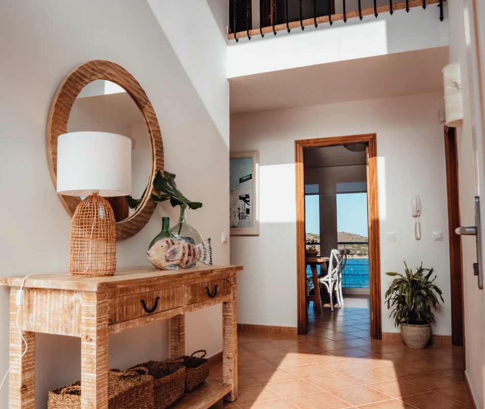 Entrada luminosa con espejo, consola de madera y vista al mar.