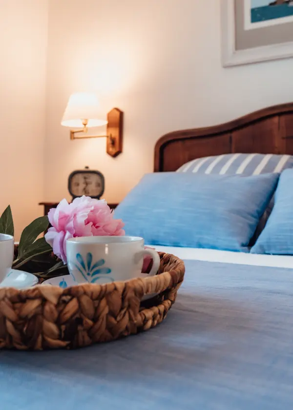 Cama azul con taza y flor en una bandeja en primer plano, l&aacute;mpara de fondo.