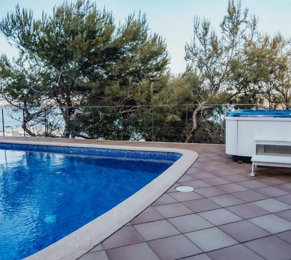 Piscina azul y jacuzzi en terraza con &aacute;rboles de fondo.