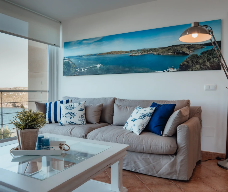 Sala con sof&aacute; gris, cojines azules y cuadro de paisaje marino en la pared.