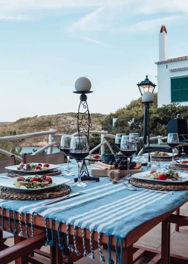 Mesa al aire libre con platos de ensalada y copas de vino, vista al fondo natural.