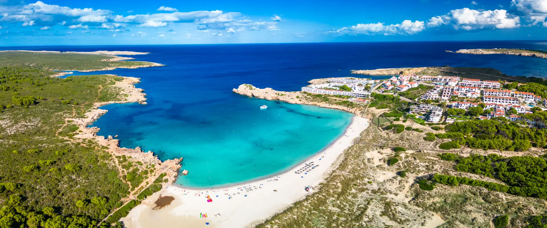 Vista a&eacute;rea de una playa con aguas turquesas y un pueblo costero al fondo.
