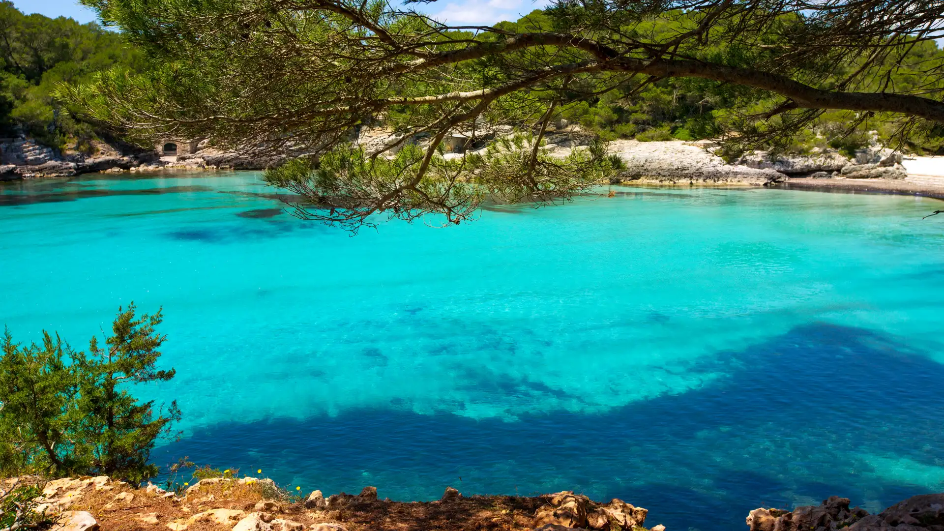 Bah&iacute;a de aguas turquesas rodeada de vegetaci&oacute;n y rocas.