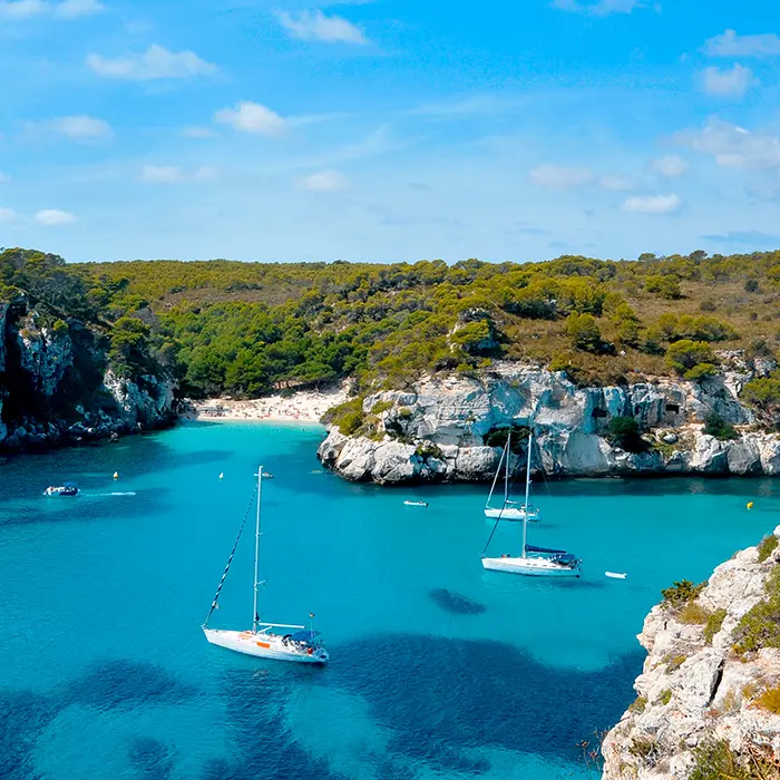 Barcos en una cala de aguas turquesas y acantilados verdes.