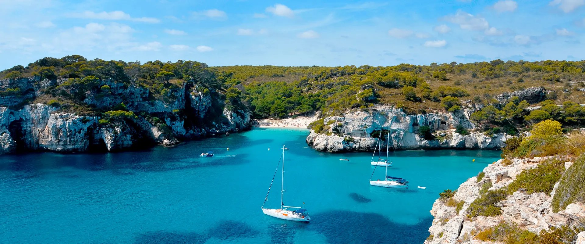 Bah&iacute;a con agua turquesa y veleros rodeados de acantilados verdes.