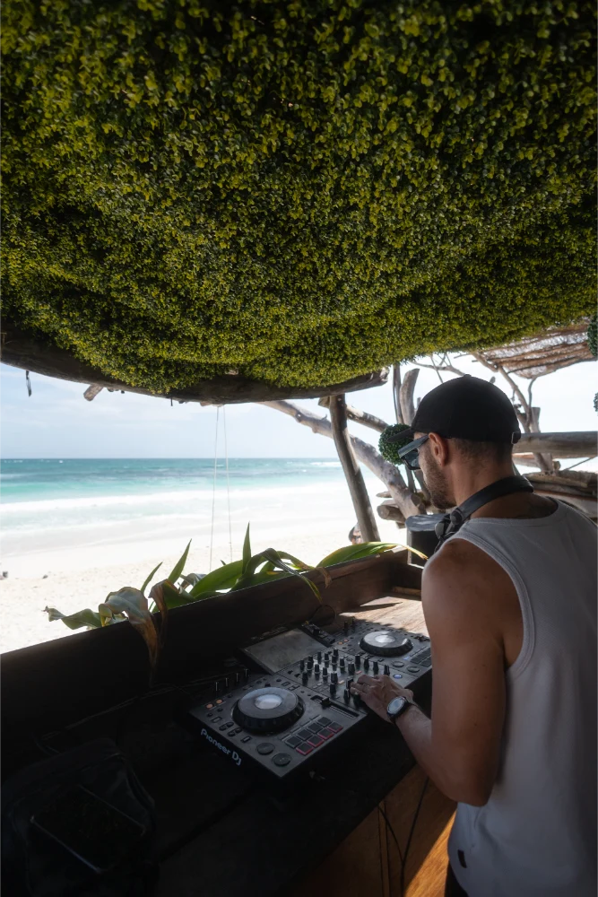 DJ playing music at a beachside booth, surrounded by nature.
