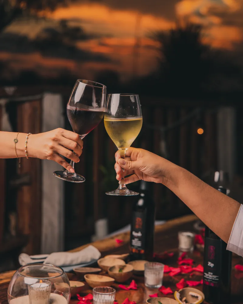 Two people clinking wine glasses at sunset over a decorated table.