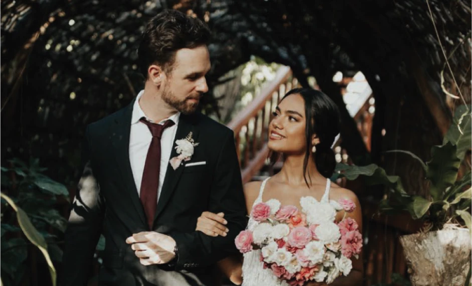 Bride and groom walking together, surrounded by greenery.