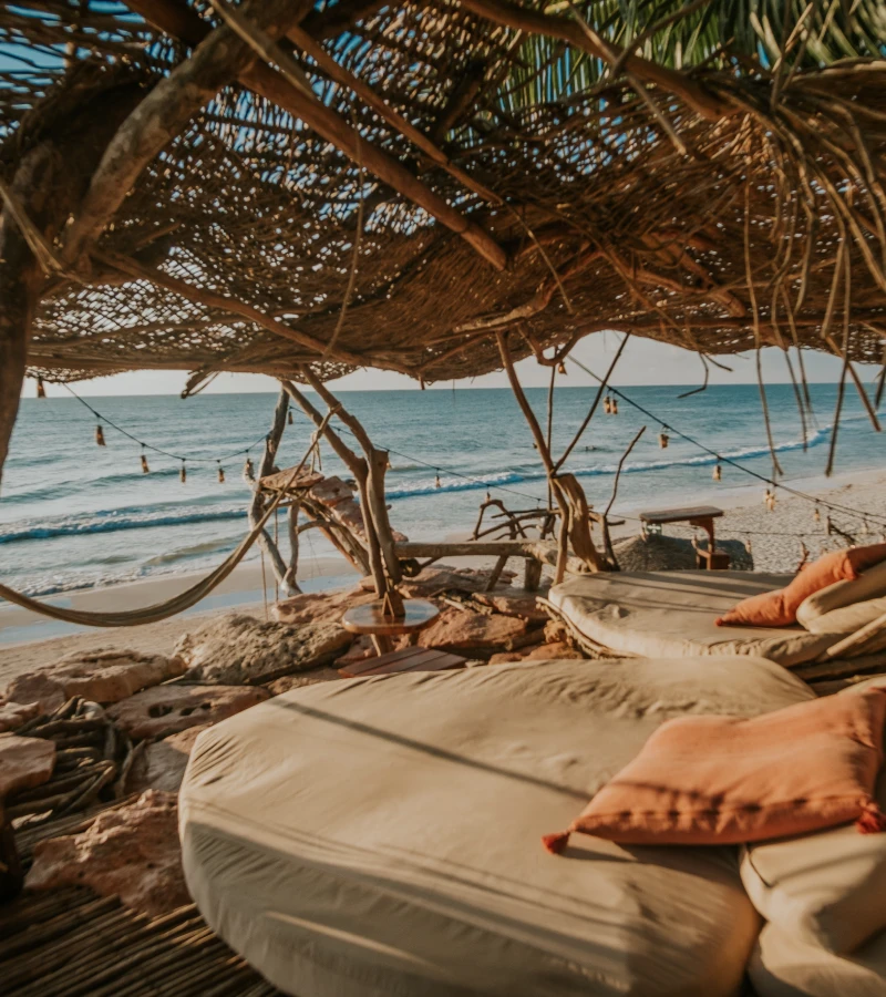 Sea view from a cozy beach cabana with rustic decor and cushions.