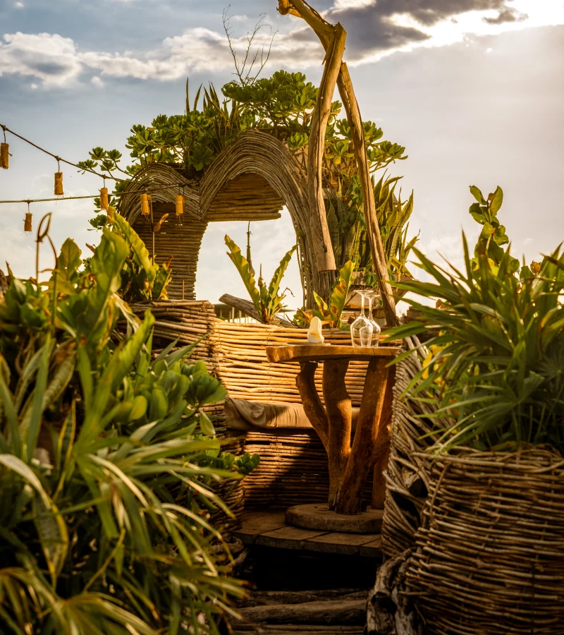 Wooden table surrounded by lush greenery under a rustic archway.