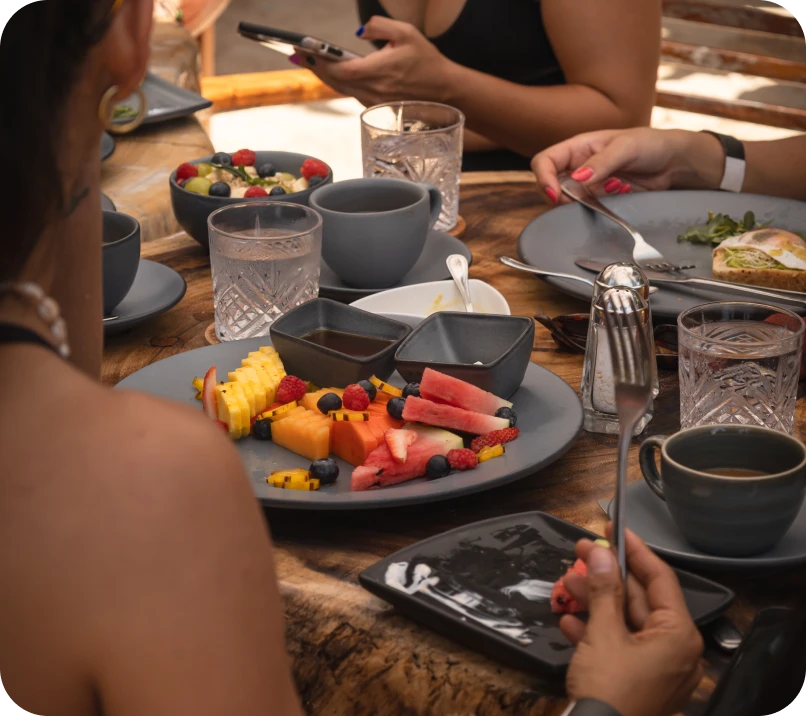 People enjoying a table with assorted fruits and drinks.