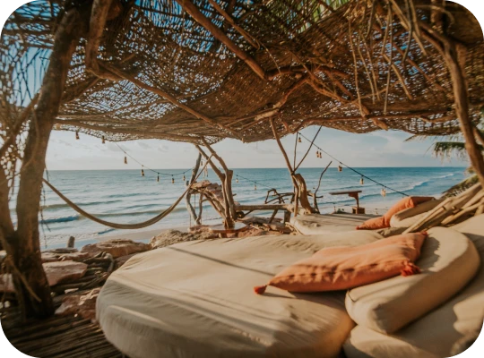 Rustic beach cabana with round loungers facing the ocean.