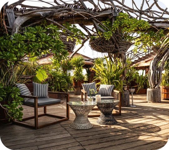 Wooden outdoor seating area with lush greenery and wicker-like decor.