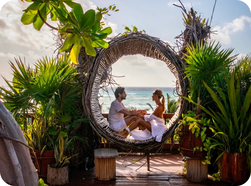 Couple sitting in a circular nest chair, ocean view in the background.