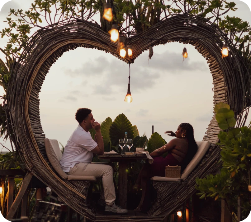 Couple dining in a heart-shaped wicker frame at sunset.