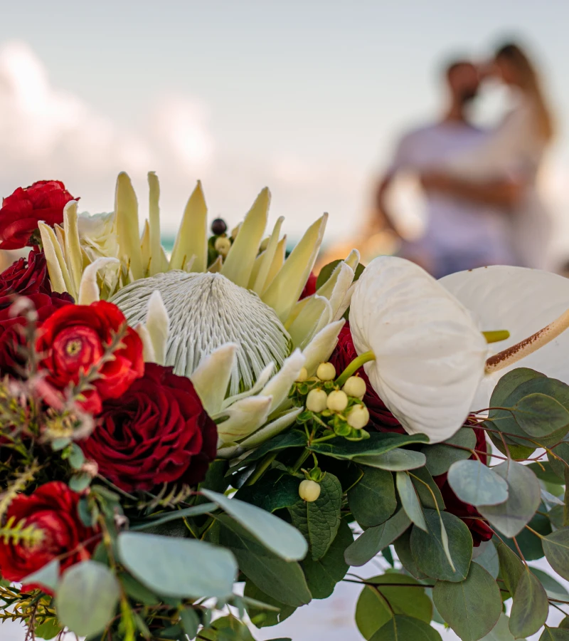 Close-up of a vibrant bouquet with a couple blurry in the background.