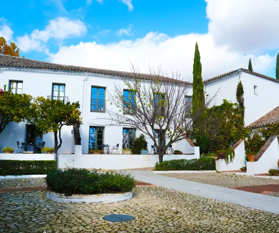 Casa blanca con jard&iacute;n y &aacute;rboles, cielo azul con nubes.