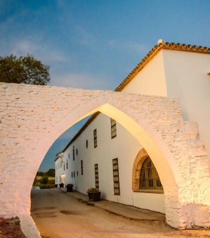 Arco de piedra blanca frente a edificio tradicional al atardecer.