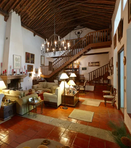 Sala de estar r&uacute;stica con chimenea, sof&aacute;s y escalera de madera.