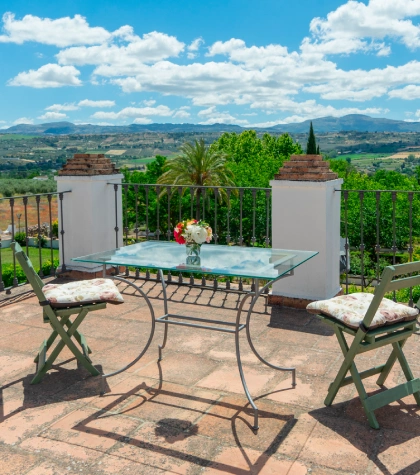 Terraza con mesa de cristal, sillas y vista panor&aacute;mica de monta&ntilde;as y &aacute;rboles.