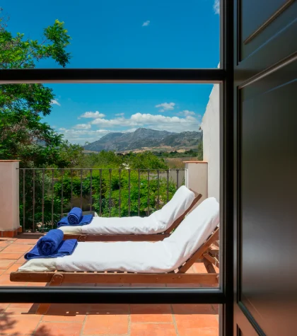 Dos tumbonas con toallas en una terraza con vistas a monta&ntilde;as y cielo azul.