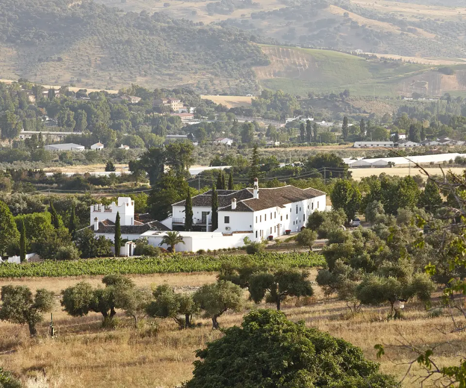 Vista de una finca blanca rodeada de &aacute;rboles y monta&ntilde;as al fondo.