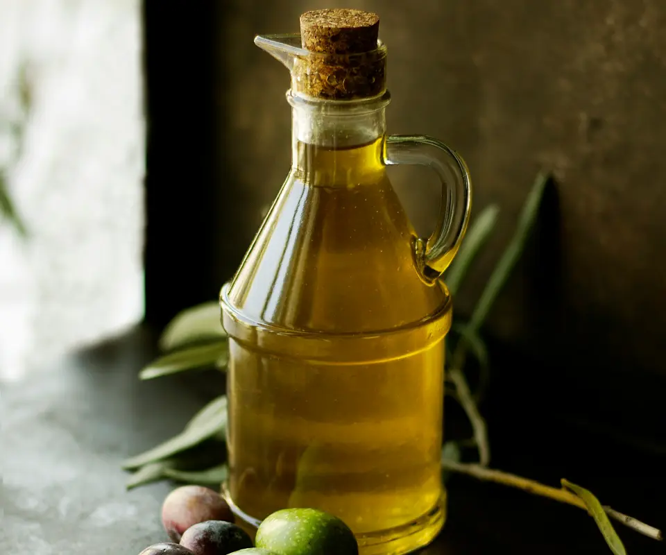 Botella de aceite de oliva con tap&oacute;n de corcho y algunas aceitunas alrededor.