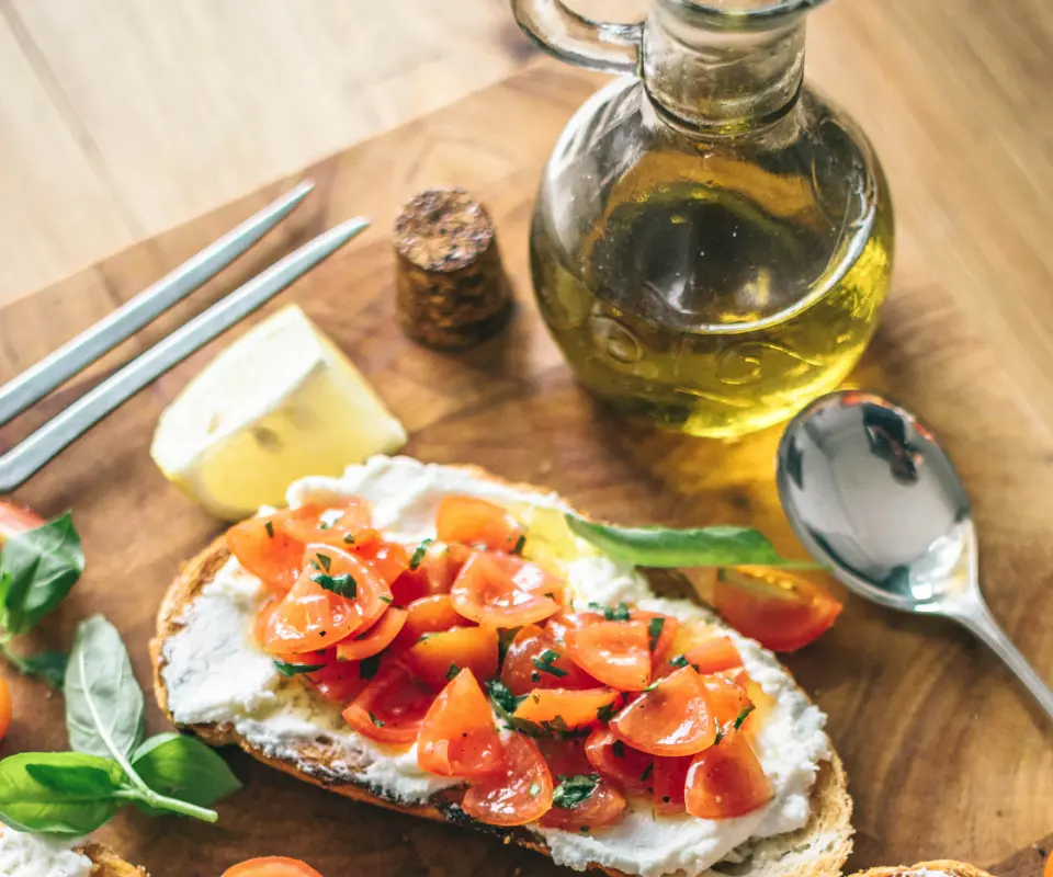 Tostada con queso, tomate y albahaca junto a una botella de aceite de oliva.