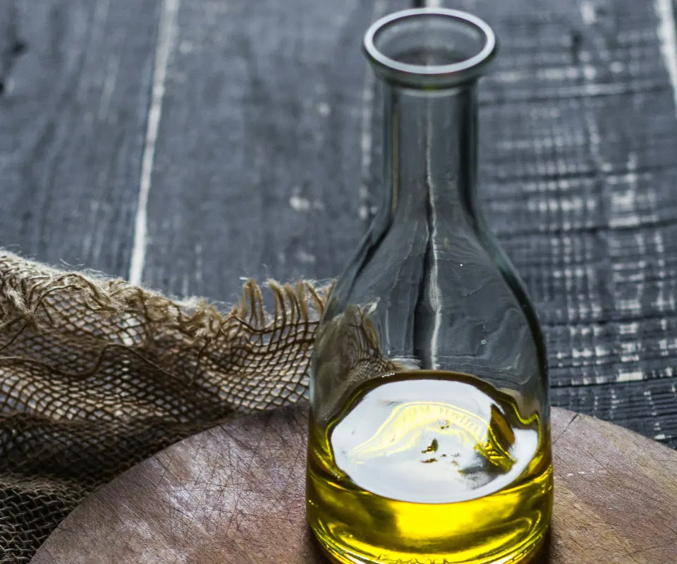 Botella de aceite sobre tabla de madera con tela r&uacute;stica al fondo.