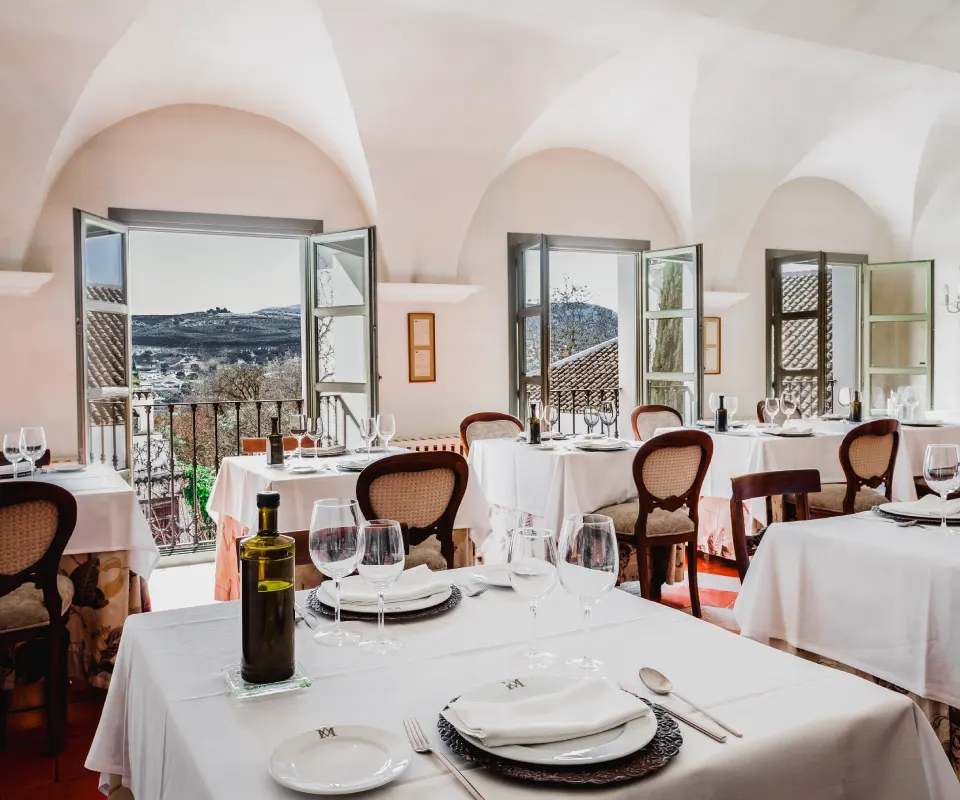 Restaurante elegante con mesas blancas y vistas panor&aacute;micas por las ventanas abiertas.