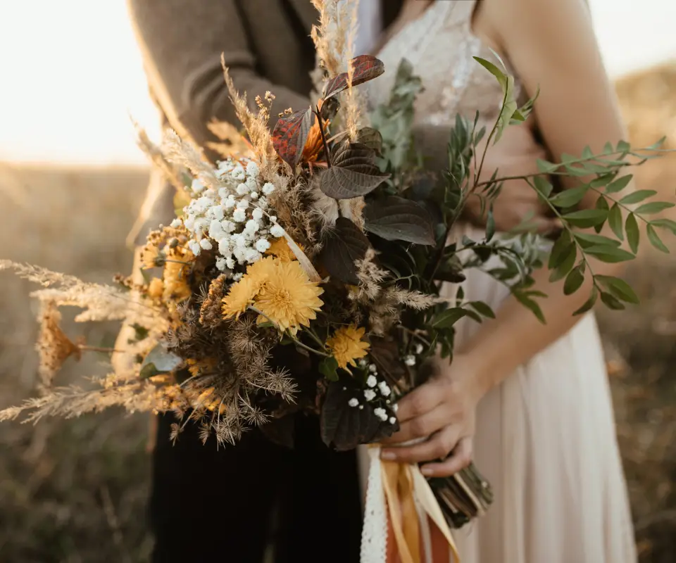 Pareja abraz&aacute;ndose al atardecer con ramo de flores silvestres.
