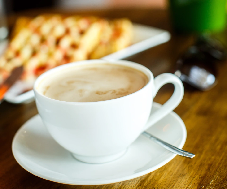 Taza de caf&eacute; con leche en una mesa de madera, fondo desenfocado.