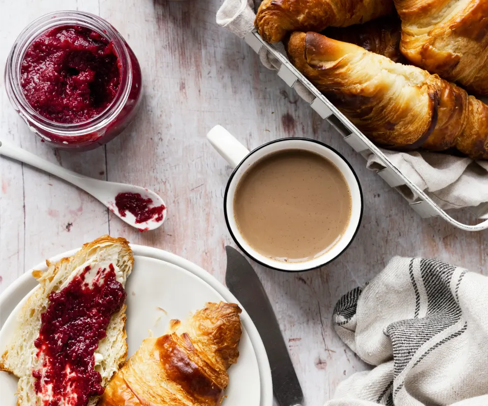 Croissants, caf&eacute; y mermelada de frambuesa sobre una mesa de madera.