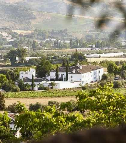 Vista de un edificio blanco rodeado de campos y &aacute;rboles en un paisaje rural.