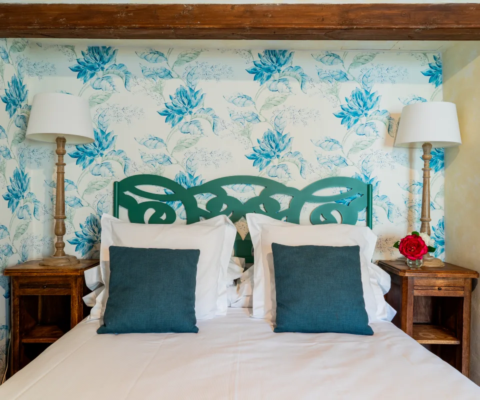 Cama doble con cojines azules, l&aacute;mparas y papel tapiz floral azul.