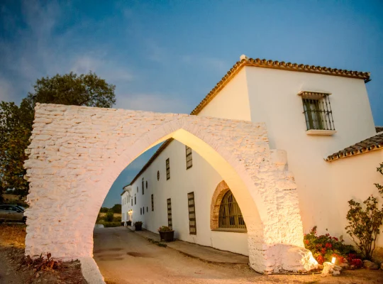 Arco de piedra frente a un edificio blanco al atardecer.