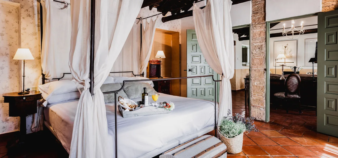 Habitaci&oacute;n acogedora con cama con dosel, desayuno y puertas abiertas al sal&oacute;n.
