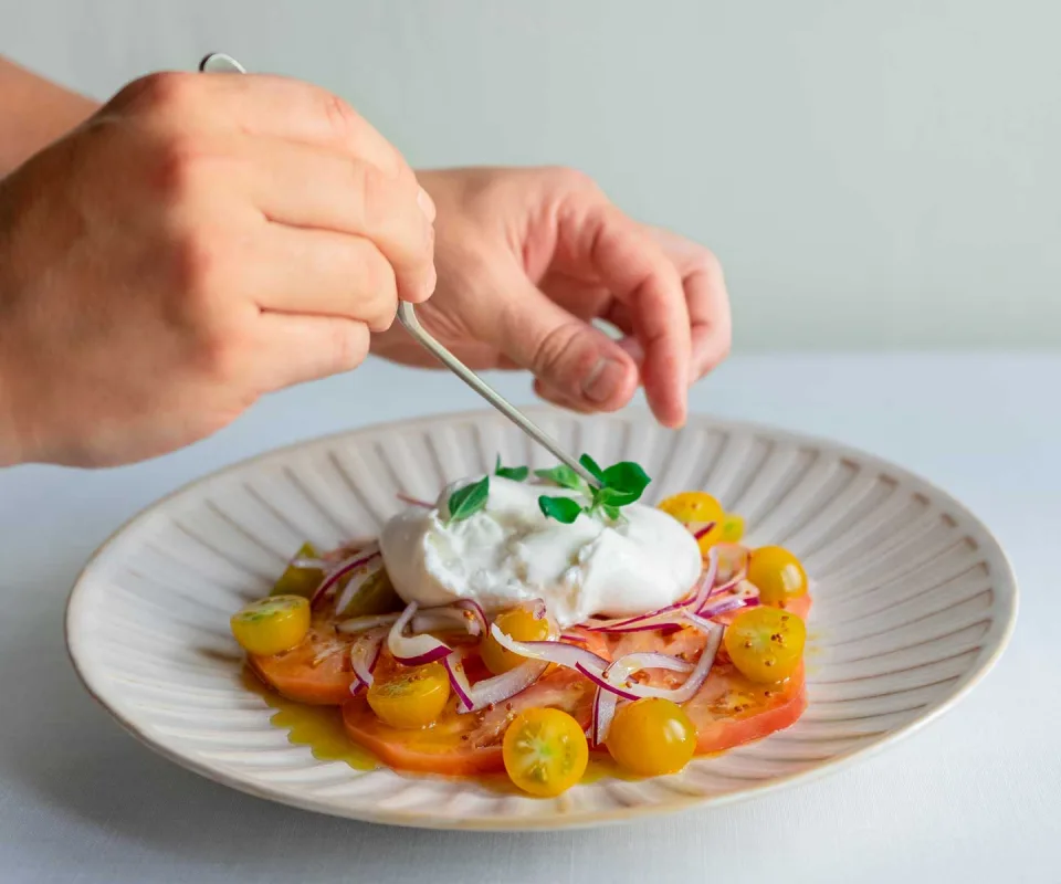 Manos decoran un plato con ensalada de tomate, queso y albahaca.