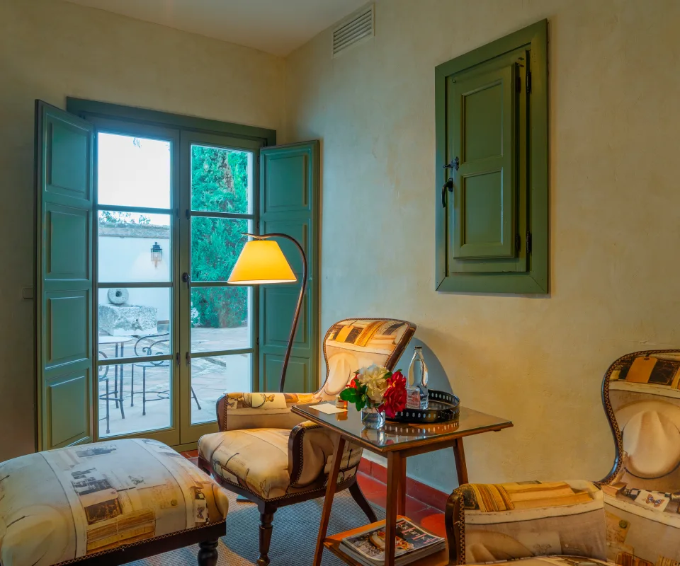 Sala con sillones, l&aacute;mpara y ventana abierta a un patio.