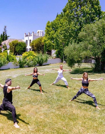 Personas practicando yoga al aire libre en un jard&iacute;n soleado.
