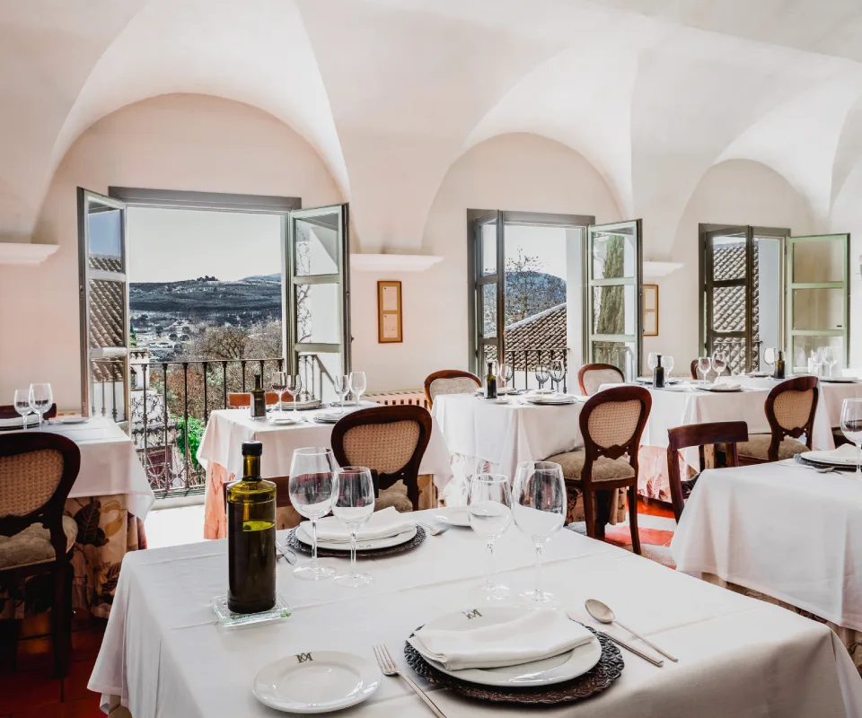 Restaurante elegante con mesas vestidas, botellas y una vista panor&aacute;mica exterior.