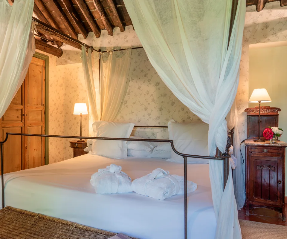 Cama con dosel y l&aacute;mparas de noche en habitaci&oacute;n r&uacute;stica acogedora.