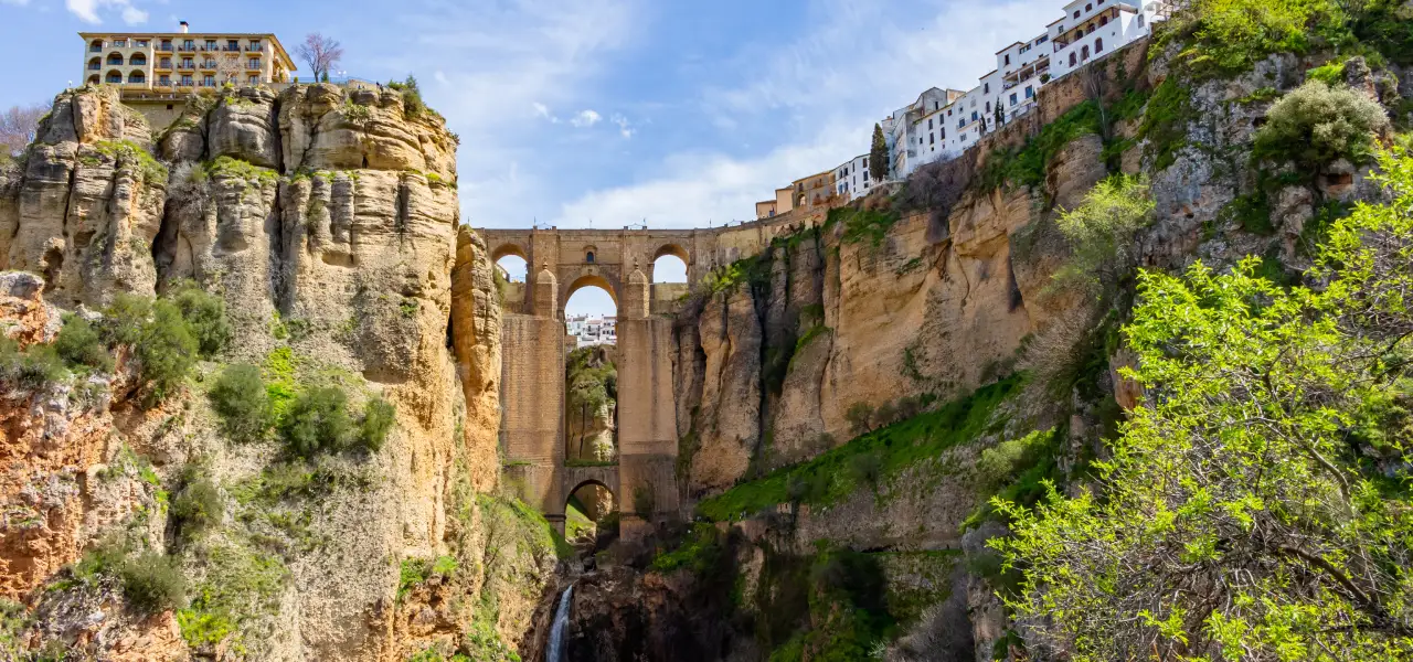 Puente sobre un desfiladero con casas en lo alto y vegetaci&oacute;n alrededor.