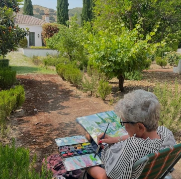 Persona pintando en un jard&iacute;n con una casa blanca al fondo.