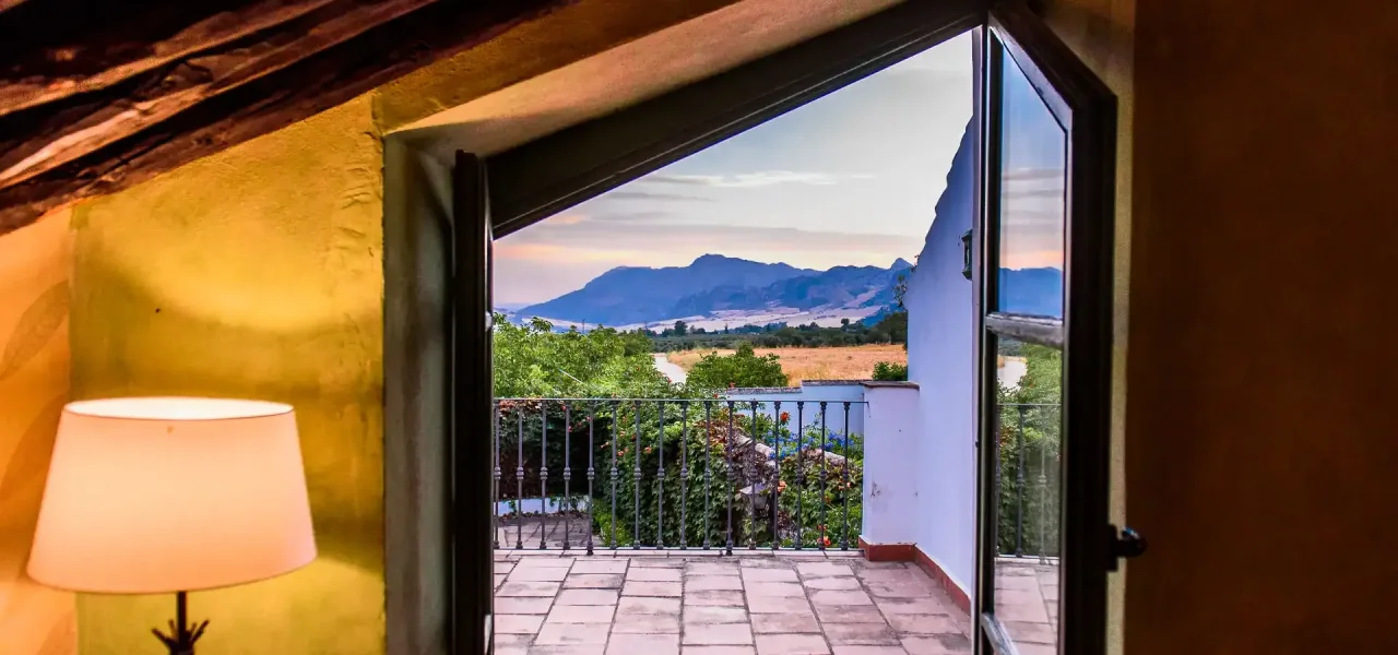 Vista de una terraza con monta&ntilde;as al fondo al atardecer desde el interior.