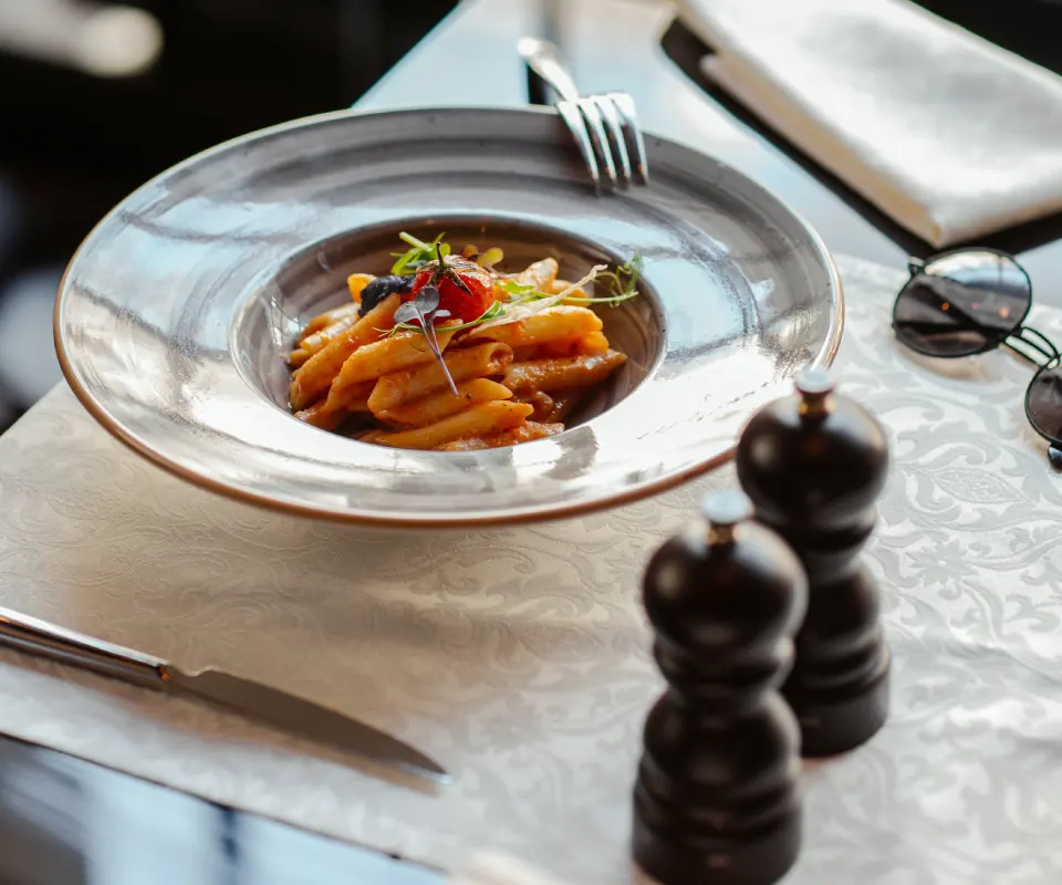 Plato de pasta con salsa en mesa elegante con cubiertos y especieros.